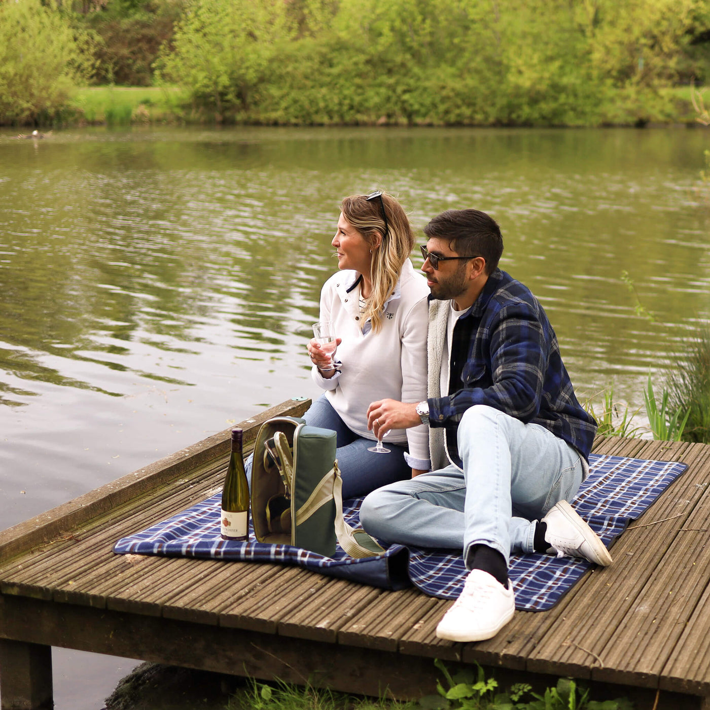 couple having picnic by river on a picnic blanket with wine cooler